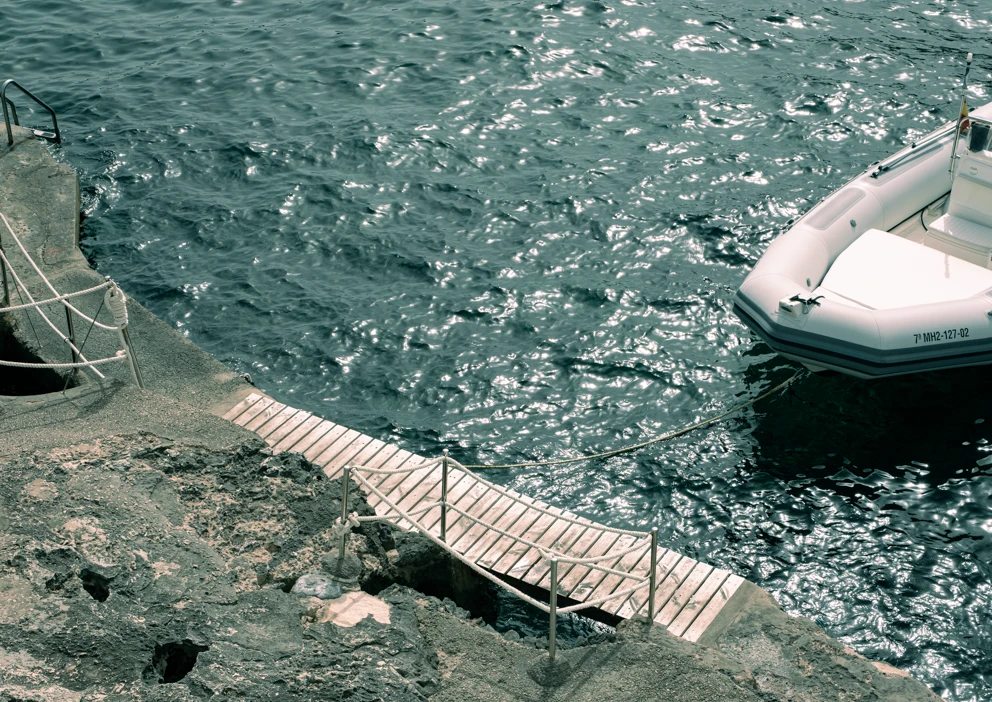 A wooden jetty over rocks beside a moored boat on glittering dark water